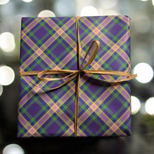 Op de afbeelding: Een cadeaudoos ingepakt in paars, groen, geel en roze geruit cadeaupapier met een bruin lint gebonden in een strik.