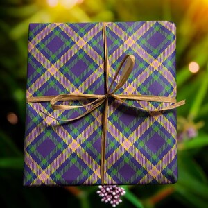 Op de afbeelding: Een paarse cadeaudoos met een geruit patroon in tinten groen, geel en roze. De doos is vastgebonden met een gouden lint.