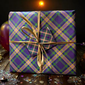 Op de afbeelding: Een paarse, groene en gele geruite cadeaudoos met een gouden lint en strik. De doos is ingepakt in een geruit patroon en vastgebonden met een gouden lint.