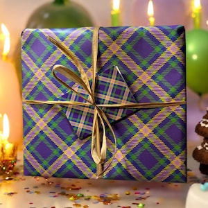 Op de afbeelding: Een paarse, groene en gele geruite cadeaudoos met een gouden lint en strik. De doos is ingepakt in decoratief papier met een geruit patroon.