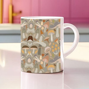 May include: A white ceramic mug with a handle features a pattern of colorful mushrooms and leaves on a light gray background.