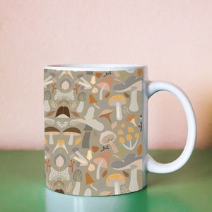 May include: A white ceramic mug with a handle. The mug has a pattern of colorful mushrooms and leaves on a light green background.