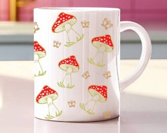 May include: White ceramic mug with a red and white mushroom pattern. The mushrooms are outlined in gold and have a white stem. There are also small gold butterflies scattered throughout the pattern.