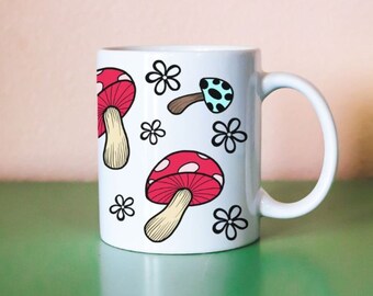 May include: White ceramic mug with a red and white mushroom design. The mug has a black outline and a black handle.