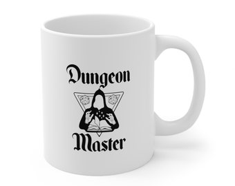 May include: White ceramic mug with a black graphic of a robed figure holding dice over an open book, inside a triangle with dice symbols. The words "Dungeon Master" are above and below the graphic in a gothic font.