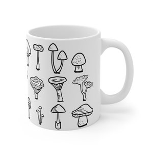 May include: White ceramic mug featuring a black and white illustration of various mushroom species. The design includes detailed drawings of different mushroom types, perfect for a nature or botany enthusiast. The mug has a standard handle for easy gripping.