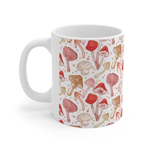 May include: White ceramic mug with a pattern of red, pink, and brown mushrooms on a white background.