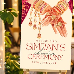 May include: A welcome sign for a wedding ceremony with a red and gold design. The sign says "Welcome to Simran's Choora Ceremony 29th June 2024".