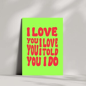 May include: A neon green poster with the words "I LOVE YOU I LOVE YOU I TOLD YOU I DO" in red, bubble-style font. The poster is leaning against a white wall.