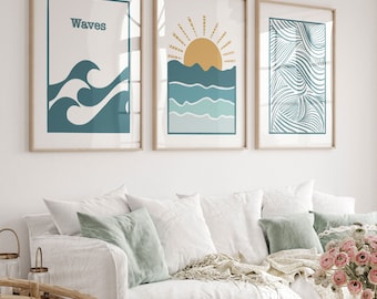 Puede incluir: Tres láminas enmarcadas con temática costera. Las láminas presentan olas oceánicas, un sol sobre el mar y patrones de olas abstractas en tonos turquesa y dorado. Los marcos son de color marrón claro, sobre un sofá blanco.