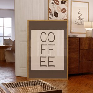 以下が含まれることがあります： 白い背景に黒い文字で「COFFEE」と書かれた額装されたプリント。フレームは茶色の木で、プリントは白い壁にかけられています。