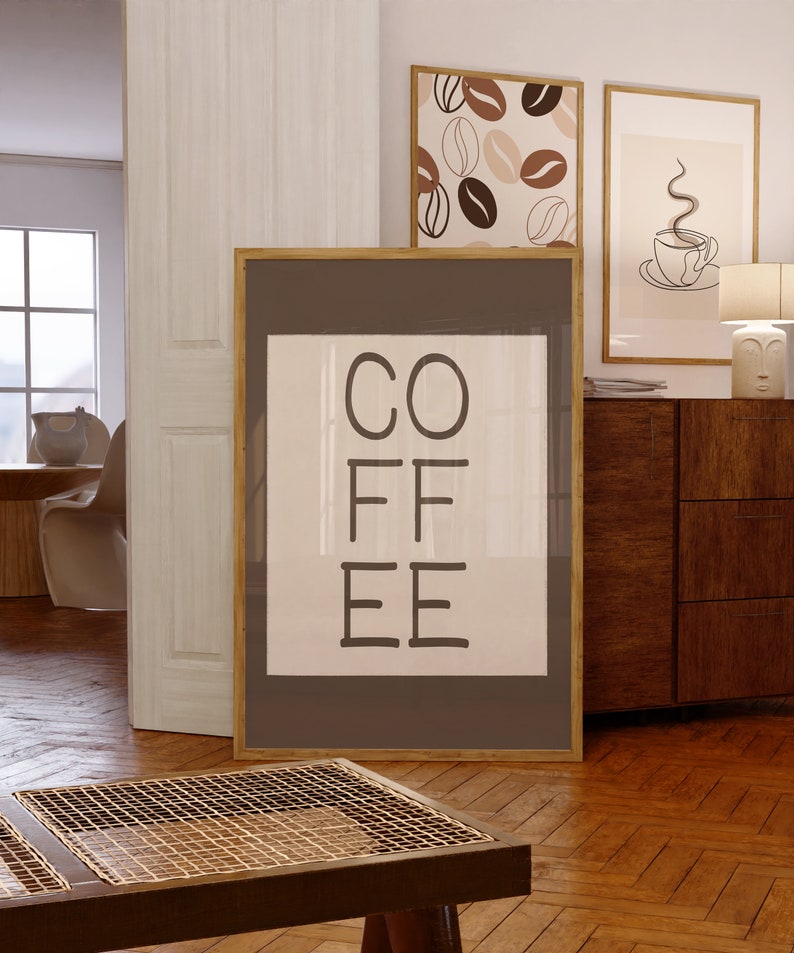 以下が含まれることがあります： 白い背景に黒い文字で「COFFEE」と書かれた額装されたプリント。フレームは茶色の木で、プリントは白い壁にかけられています。