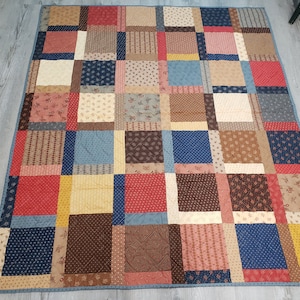 May include: A patchwork quilt featuring a mix of floral and geometric patterns in shades of red, brown, blue, and yellow.
