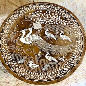May include: Round, brown wooden decorative tray with a detailed peacock and bird design. The birds are white with intricate detailing, set against a brown background. The tray has a decorative white border.