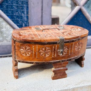May include: A wooden box with intricate carvings and a metal latch. The box is oval shaped and sits on four short legs.