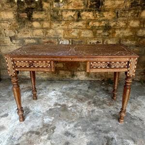 Puede incluir: Un escritorio de madera con intrincados diseños de nácar incrustados. El escritorio tiene tres cajones y patas torneadas.