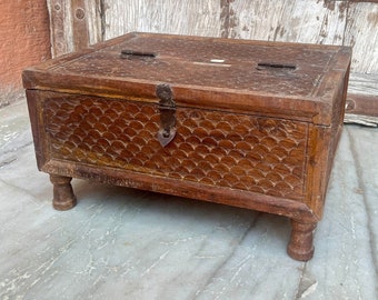 May include: A wooden box with a carved design and a metal latch. The box has four legs and is made of dark brown wood.