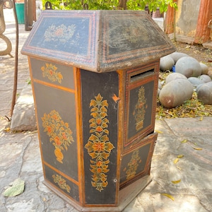 May include: A black wooden box with intricate floral designs painted in orange, yellow, and green. The box has a hinged lid and a small opening on the front.
