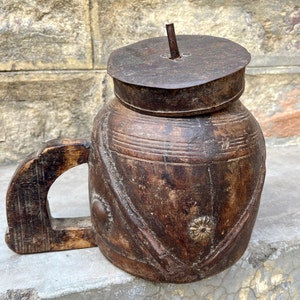 Könnte beinhalten: Eine braune Wasserkanne aus Holz mit einem Metalldeckel und einem geschnitzten Design. Die Kanne hat einen Griff und ist aus dunklem Holz gefertigt.