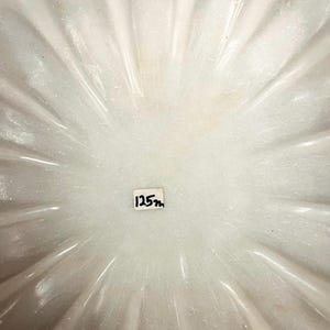 May include: A white, fluted bowl with a radial pattern. The bowl has a smooth, shiny surface. The text "125m" is written on a small white label in the centre of the bowl.