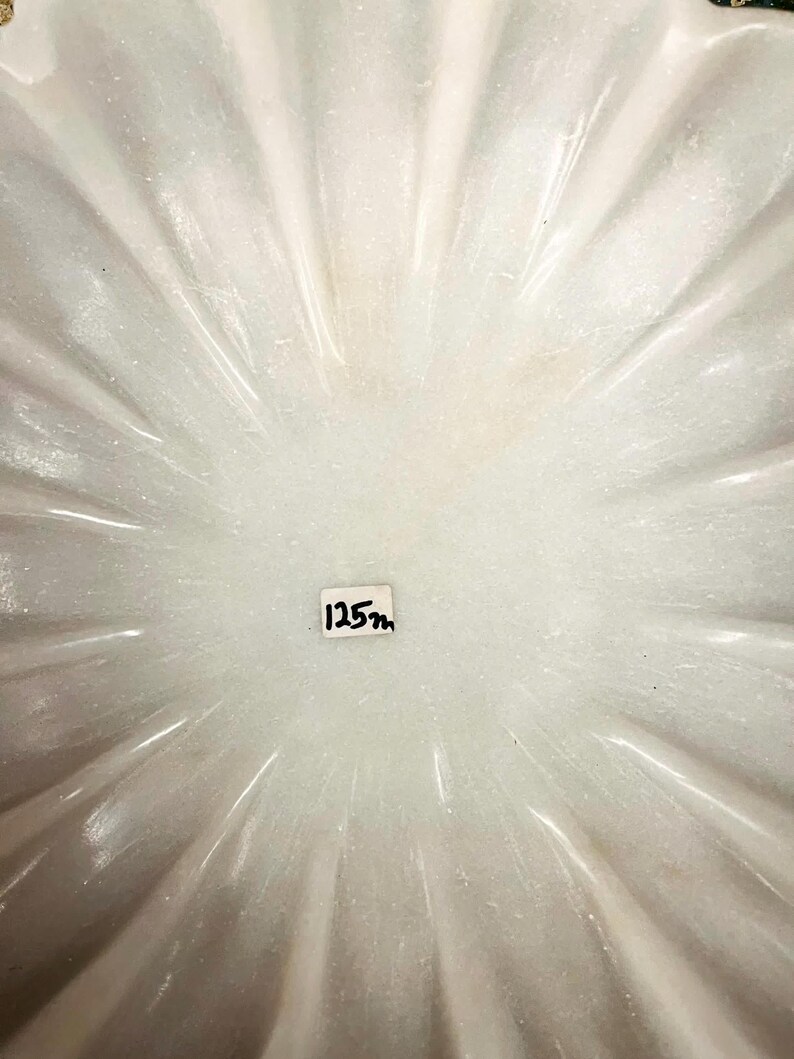 May include: A white, fluted bowl with a radial pattern. The bowl has a smooth, shiny surface. The text "125m" is written on a small white label in the centre of the bowl.