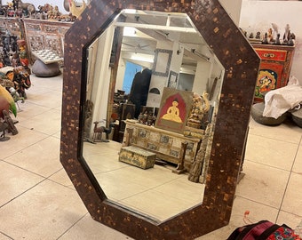 May include: Octagonal mirror with a brown mosaic frame. The mirror reflects a room with various decorative items, including a painting of a person in a seated pose.