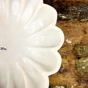 May include: A white, petal-shaped decorative dish. The dish has a glossy finish and a scalloped edge. The background is a rustic wooden surface with hints of blue and green paint.