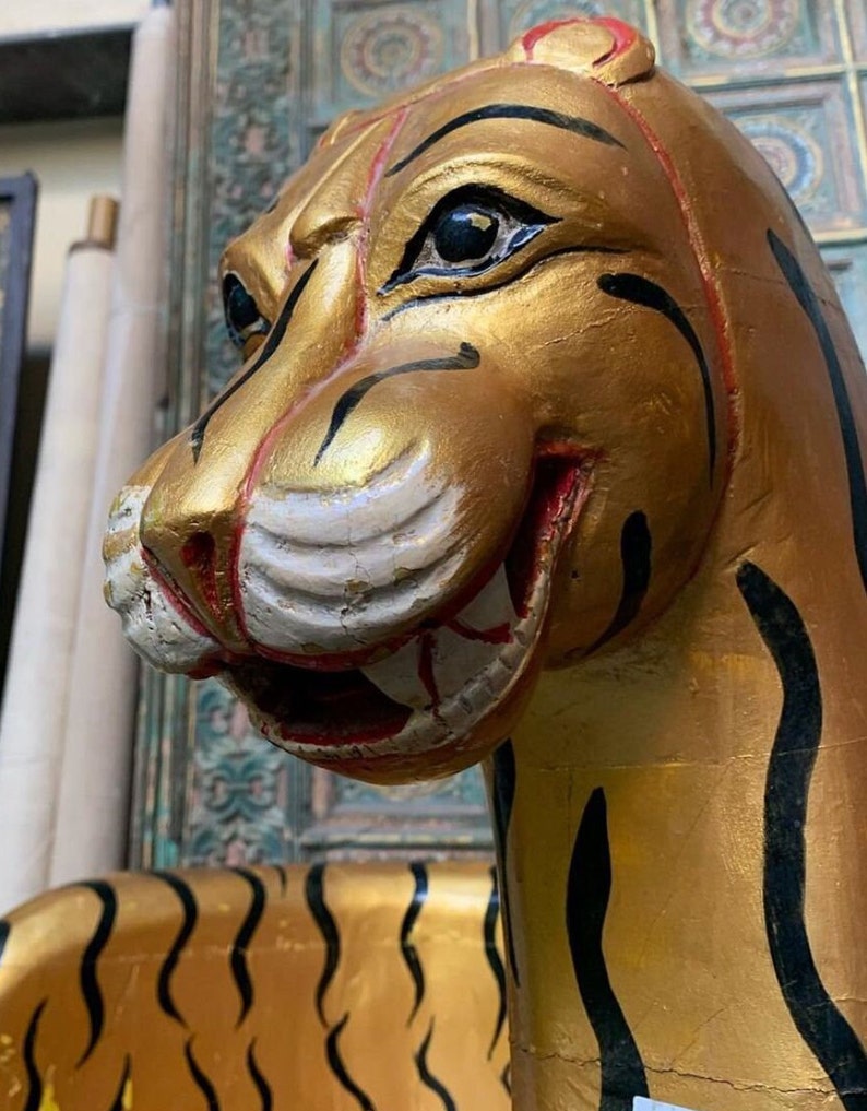 May include: A golden tiger statue with black stripes, painted with red accents around the mouth and eyes. The tiger's head is turned to the side, and its mouth is slightly open, revealing its teeth.