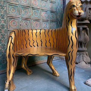May include: A wooden chair shaped like a tiger, painted gold with black stripes. The chair has a seat and a back, and the legs are carved to look like tiger paws.