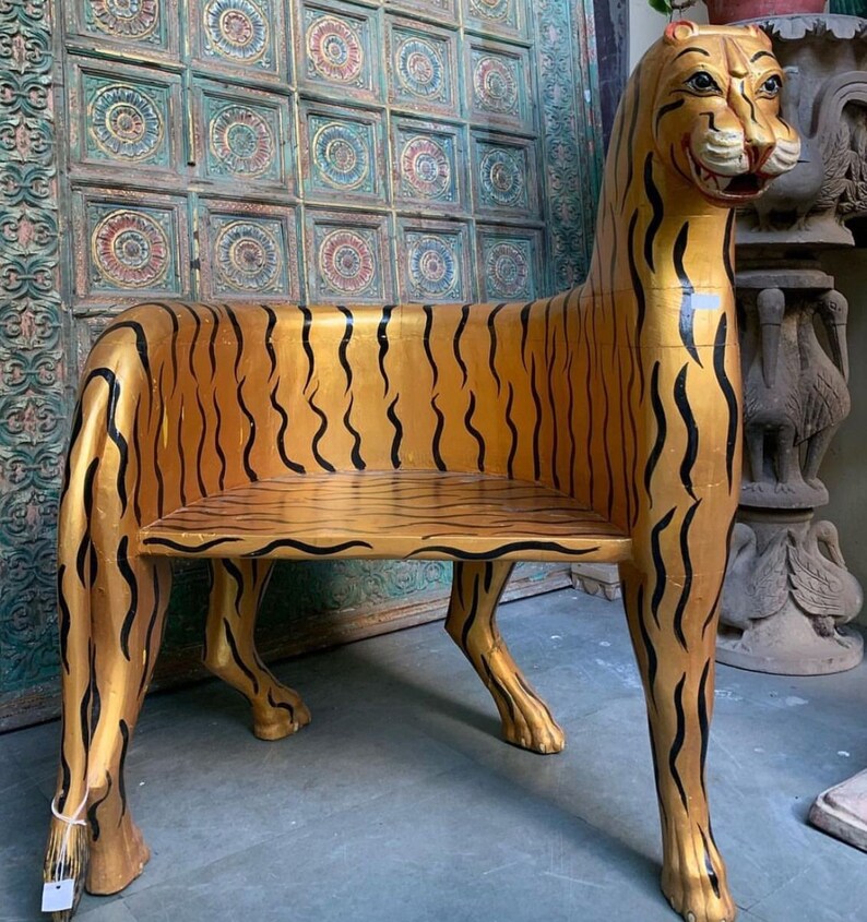 May include: A wooden chair shaped like a tiger, painted gold with black stripes. The chair has a seat and a back, and the legs are carved to look like tiger paws.