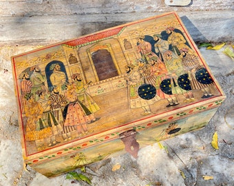 May include: A wooden box with a hinged lid, painted with a scene of people in traditional clothing. The box is decorated with intricate details and has a gold-coloured latch.