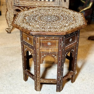 May include: Octagonal wooden table with intricate inlaid mother of pearl designs. The table has a drawer and a carved base.