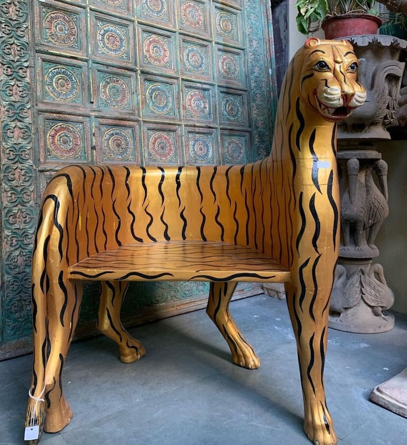 May include: A wooden chair shaped like a tiger, painted gold with black stripes. The chair has a seat and a back, and the legs are carved to look like tiger paws.