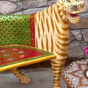 May include: A hand-painted wooden bench shaped like a tiger. The bench is painted in gold, white, and green stripes. The seat is red with a floral design. The bench is a unique and decorative piece of furniture.