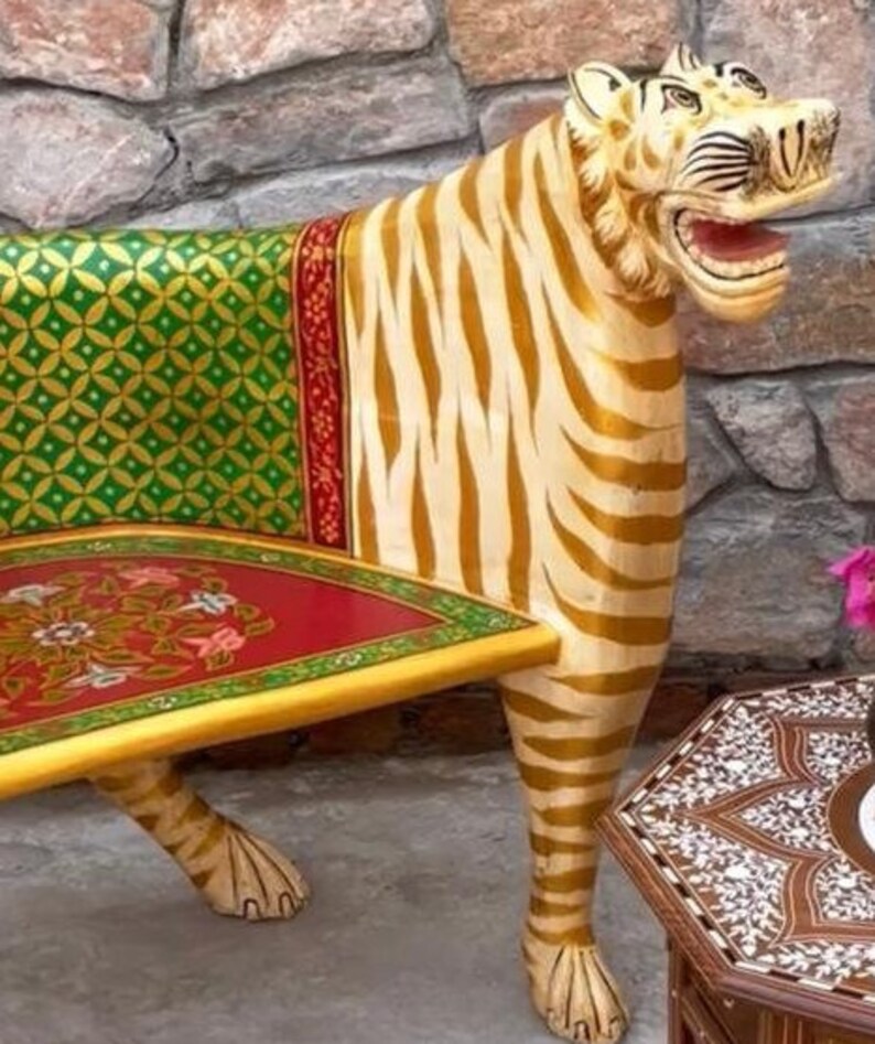 May include: A hand-painted wooden bench shaped like a tiger. The bench is painted in gold, white, and green stripes. The seat is red with a floral design. The bench is a unique and decorative piece of furniture.