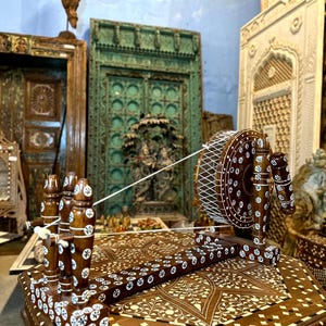 Pode incluir: Uma roda de fiar de madeira com intrincados desenhos de incrustações brancas. A roda está sentada em uma mesa com um design de incrustações semelhante.