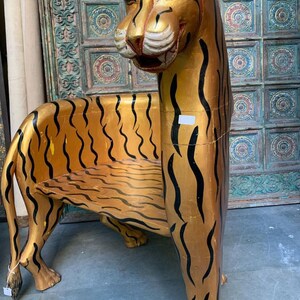 May include: A wooden chair shaped like a tiger with gold and black stripes. The chair has a seat and a back.