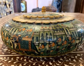 May include: A hand-painted, oval decorative box with a lid. The box depicts a procession with elephants and figures in traditional clothing. The lid and base have a floral design. The box is made of wood.