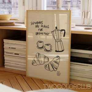 May include: A framed print with the text "Sundays are made for breakfast" and a drawing of a coffee pot, two coffee cups, and two croissants. The print is on a light brown background and has a wooden frame.
