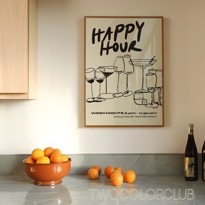 May include: A framed poster with the text "HAPPY HOUR" in black script. The poster features a black and white illustration of various glasses of wine and cocktails. The text "WEEK NIGHTS 6 PM - 11:30 PM" and "SHOULD WE GET ANOTHER DRINK?" is printed below the illustration. Two bottles of wine are on a gray countertop with a bowl of oranges.