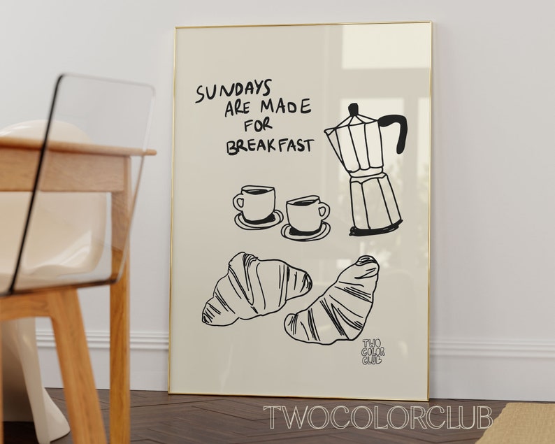 May include: A white framed print with black text that reads "Sundays are made for breakfast". The print also features a black and white illustration of a coffee pot, two coffee cups, and two croissants.