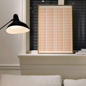 May include: A framed print with the text "NOTHING CHANGES IF NOTHING CHANGES." repeated in a light orange color on a white background. The print is hanging on a white wall above a window with white blinds.