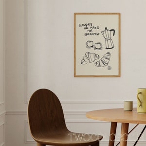 May include: A framed print featuring a black and white illustration of a coffee pot, two cups of coffee, and two croissants. The text on the print reads "Sundays are made for breakfast".