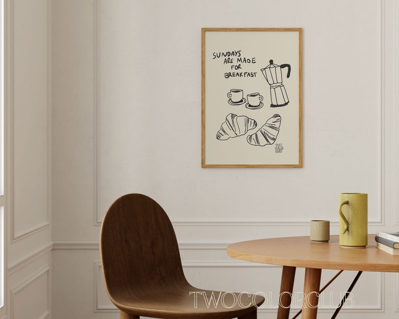 May include: A framed print featuring a black and white illustration of a coffee pot, two cups of coffee, and two croissants. The text on the print reads "Sundays are made for breakfast".