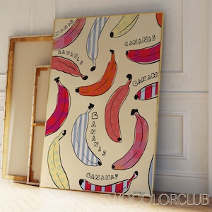 以下が含まれることがあります： クリーム色のキャンバスプリントに、カラフルなバナナのイラストが描かれています。バナナは、さまざまなパターンと色で、漫画のようなスタイルで描かれています。プリント全体に「バナナ」という文字が繰り返されています。