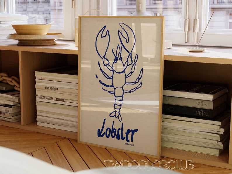 K&ouml;nnte beinhalten: Ein gerahmter Druck mit einer blauen Linienzeichnung eines Hummers auf wei&szlig;em Hintergrund. Der Text "Lobster" ist in Blau unter dem Hummer geschrieben. Der Rahmen ist in hellem Holz gehalten.