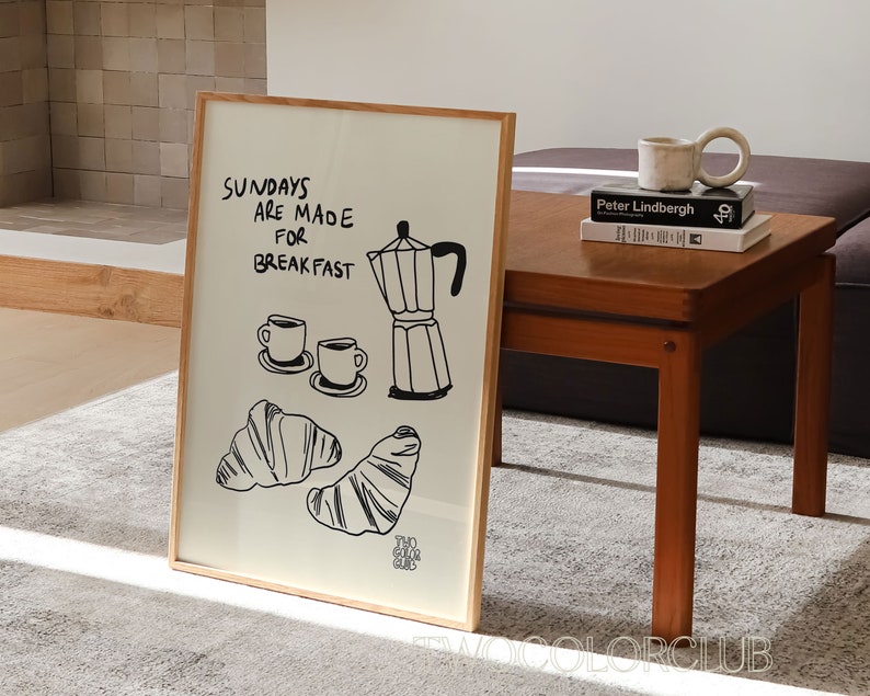 May include: A framed print with a black and white illustration of a coffee pot, two coffee cups, and croissants. The text on the print reads "Sundays are made for breakfast".