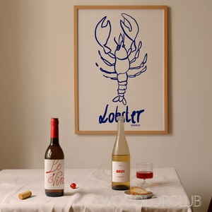K&ouml;nnte beinhalten: Ein wei&szlig;er Tisch mit einer wei&szlig;en Tischdecke, ein Korken, eine Rotweinflasche mit einem wei&szlig;en Etikett, auf dem "Le Vin" steht, eine rote Kirsche, ein klares Glas Rotwein, eine klare Flasche Wei&szlig;wein mit einem wei&szlig;en Etikett, auf dem "BRUT" steht, ein St&uuml;ck Brot auf einem kleinen wei&szlig;en Teller und ein gerahmter Druck eines blauen Hummers mit dem Wort "Lobster" darunter.