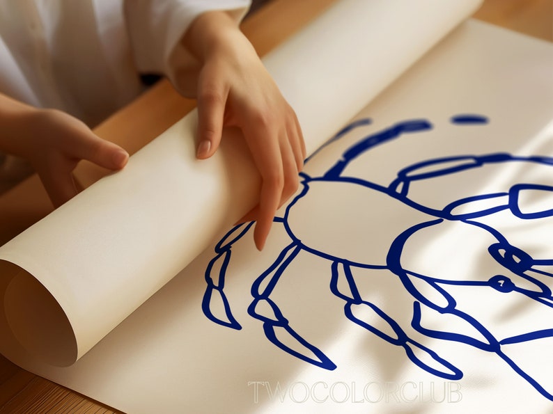 K&ouml;nnte beinhalten: Eine Person rollt ein wei&szlig;es Blatt Papier auf, auf dem eine blaue Tintenzeichnung eines Krebses zu sehen ist. Die Zeichnung ist einfach und stilisiert, die Beine und der K&ouml;rper des Krebses sind mit dicken blauen Linien umrandet. Der Text "TWOCOLORCLUB" ist unten auf dem Blatt gedruckt.