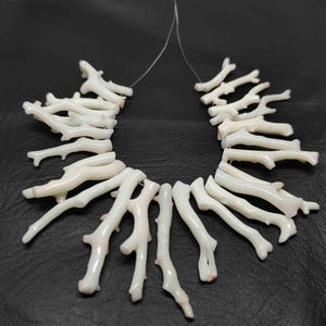 May include: A necklace composed of white coral branch beads. The coral pieces are strung together on a thin, clear cord, creating a natural and organic aesthetic. The beads have a textured surface and varying shapes.